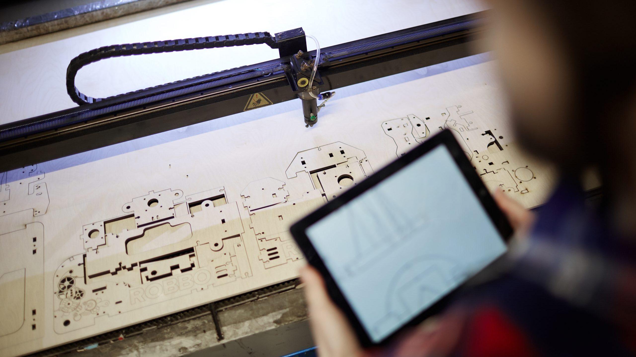 Plywood sheet with cut details and engineer with touchpad near by